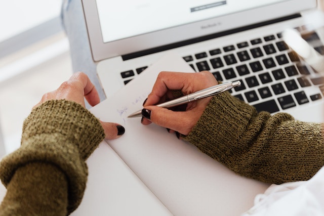 someone taking notes next to a laptop